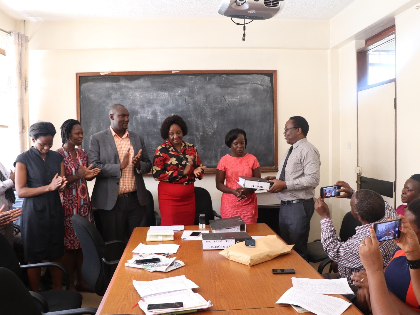 Pictured Below: Outgoing Chair, Prof Freddie Ssengooba (extreme right) hands over a file to the new Chair, Dr Elizabeth Ekirapa (next right). Looking on is the Dean (in floral top and red skirt), Mr Amos Dembe, the internal auditorr and University representative, Dr Jane Mutyoba, and Dr Esther Buregyeya, the Chair of Disease Control and Environmental Health