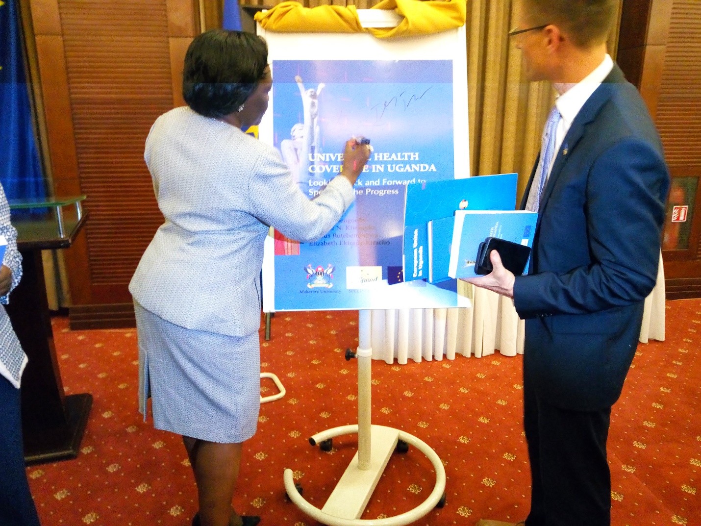 Hon Opendi autographs the dummy book cover as the EU Representative, Mr. Tiedemann looks on after he has autographed as well.
