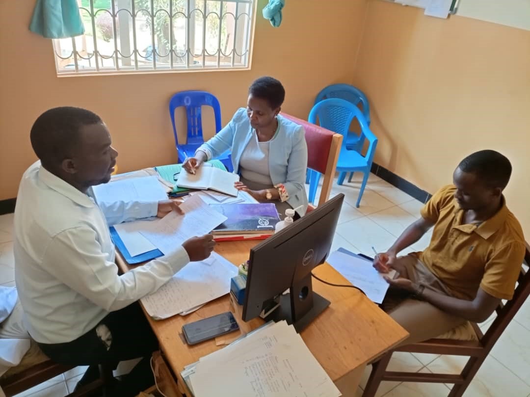 Dr. Livingstone Mujjuzi (in white shirt), the in-charge for Kira Health Centre IV discussing his progress with implementing his action points with Ms. Bonny Natukunda (in a blue coat) and Mr. Allan Ssembuusi (Project Coordinator).