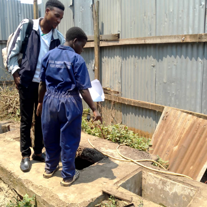 Christopher Tumusiime (left) a research assistant being shown by a sanitation worker some of the hazards when working around a septic tank