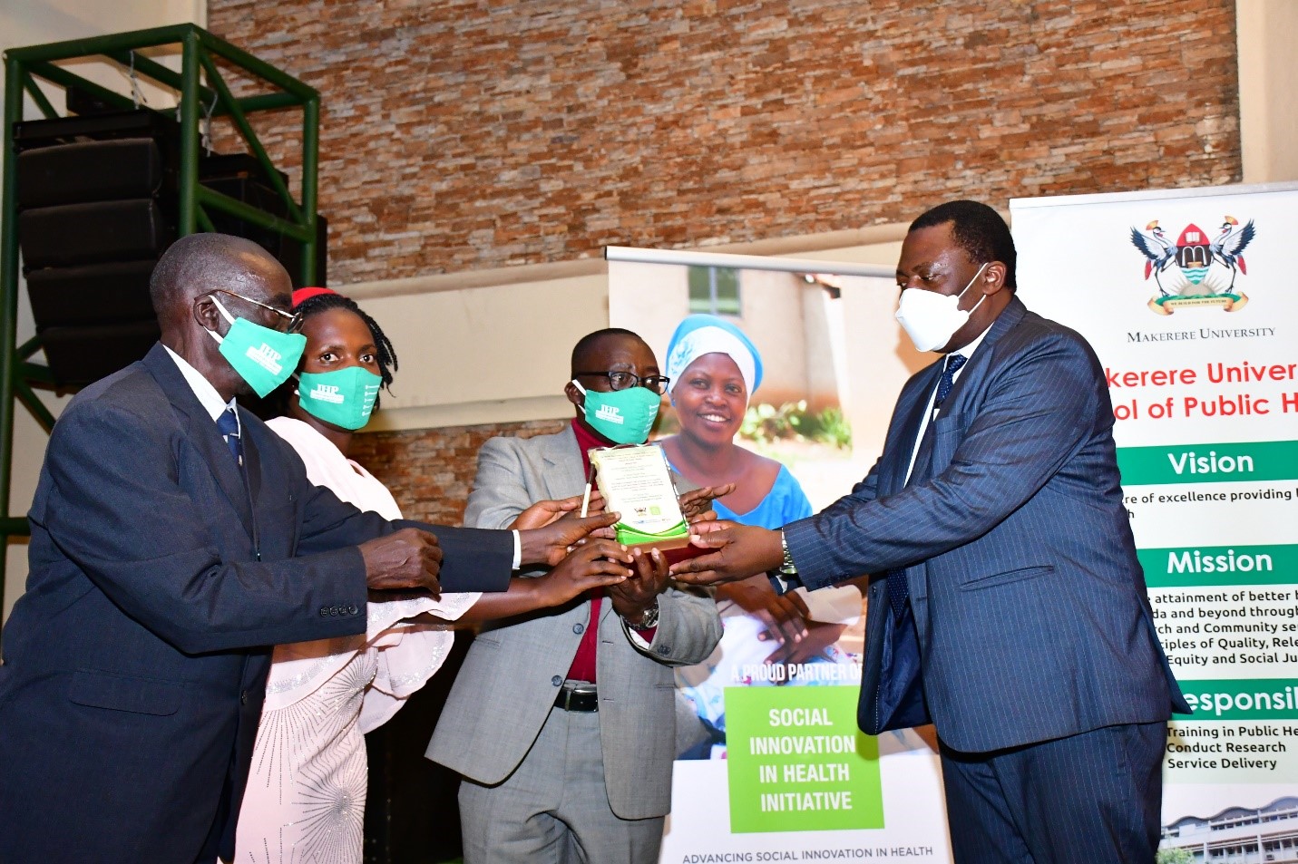 Dr. Olaro Charles, Director Clinical Services at Ministry of Health hands over a plaque to Dr. Manasseh Tumuhimbise and colleagues from Ishaka Health Plan, the winners of the 2020 Social Innovations in Health Awards organized by the School of Public Health. 