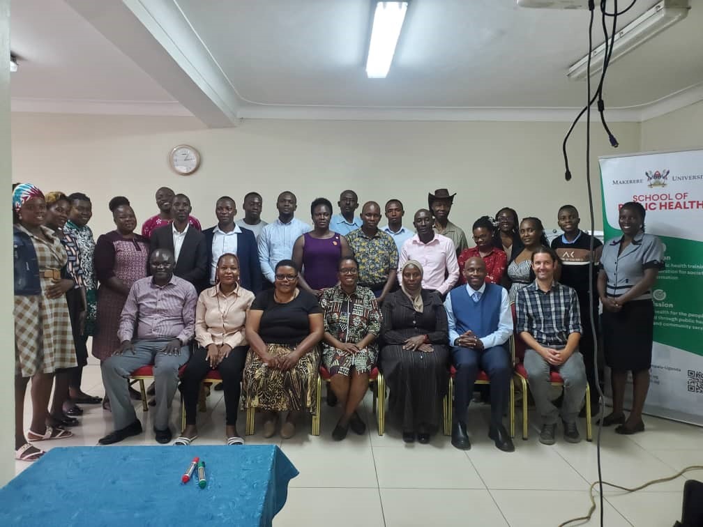 A group photo taken at the end of the workshop including Dr. Catherine Sebuguzi (in kitenge dress at the front), Dr. David Musoke (in blue sleeveless sweater), and Dr. Kevin Deane (in checked shirt at the front).