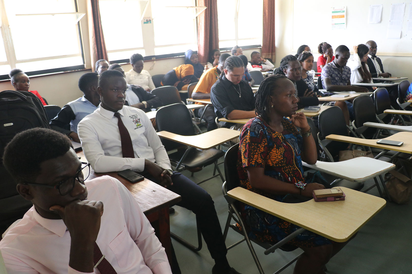 students listening attentively to presentation by  JHU-Makerere Peer to Peer Learning Team
